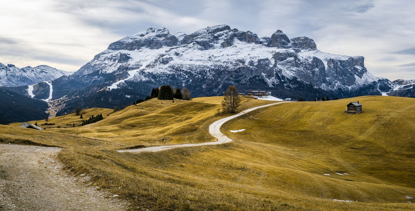 Dolomites Mountains | Body Feels A winding path leads toward snow-capped mountains under a cloudy sky, evoking feelings of inner peace.
